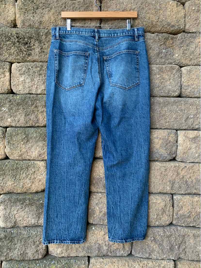 Blue denim jeans with a straight leg and back pockets hanging against a stone wall.