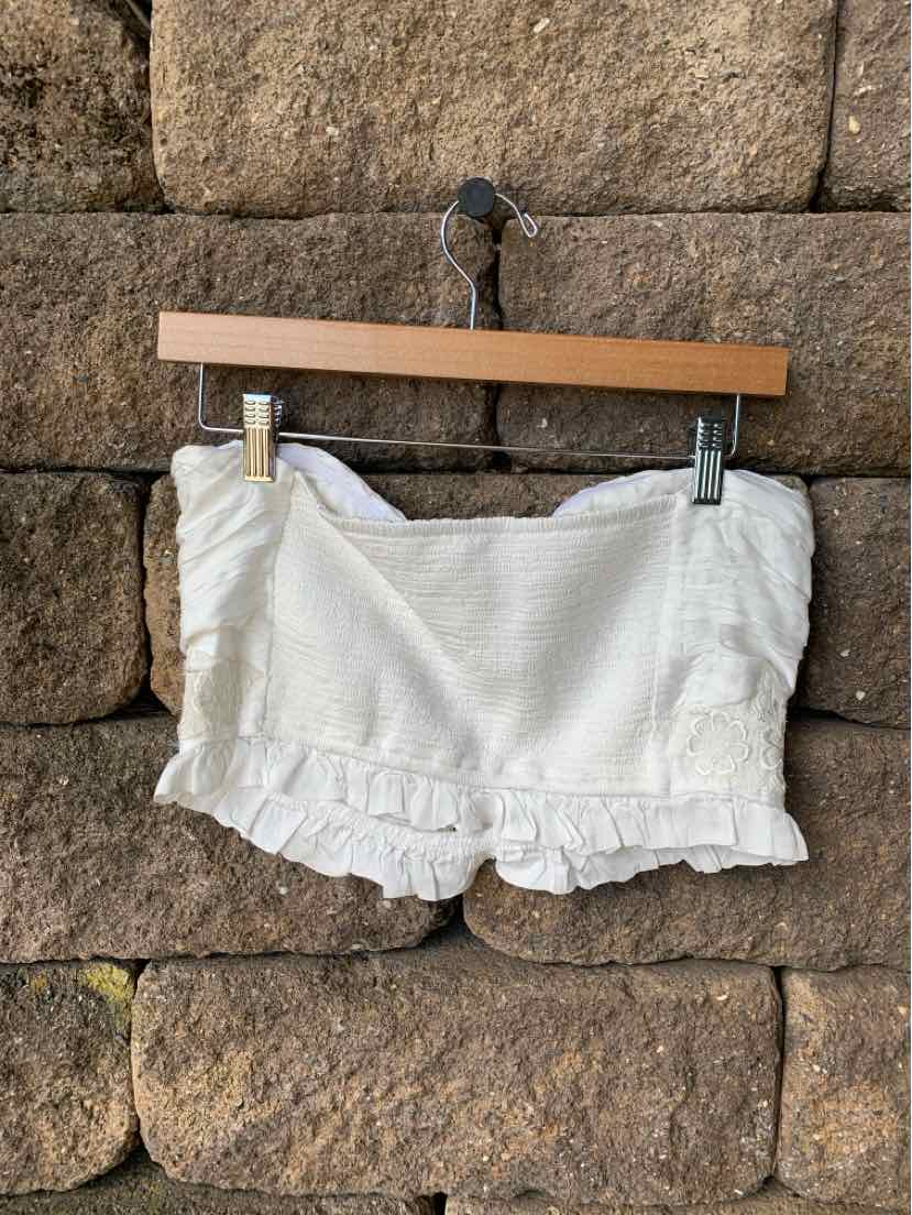 White cropped bandeau top with ruffled hem and textured fabric hanging on wooden hanger.