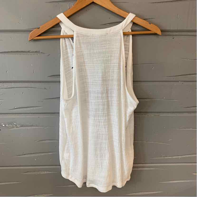 White sleeveless knit tank top with wide shoulder straps hanging on wooden hanger.
