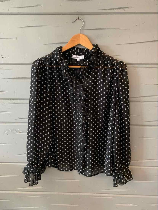 Black long-sleeve blouse with white polka dots, ruffled cuffs, and button-down front.