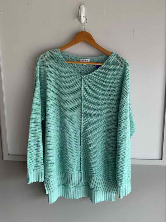 Light blue knit sweater with ribbed cuffs and hem hanging on wooden hanger against white door.