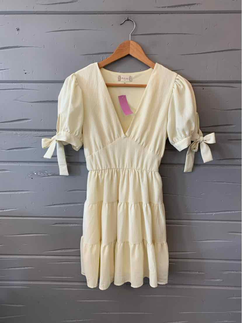 Cream-colored short dress with puff sleeves and tie details at cuffs, cinched waist, and flowy skirt.