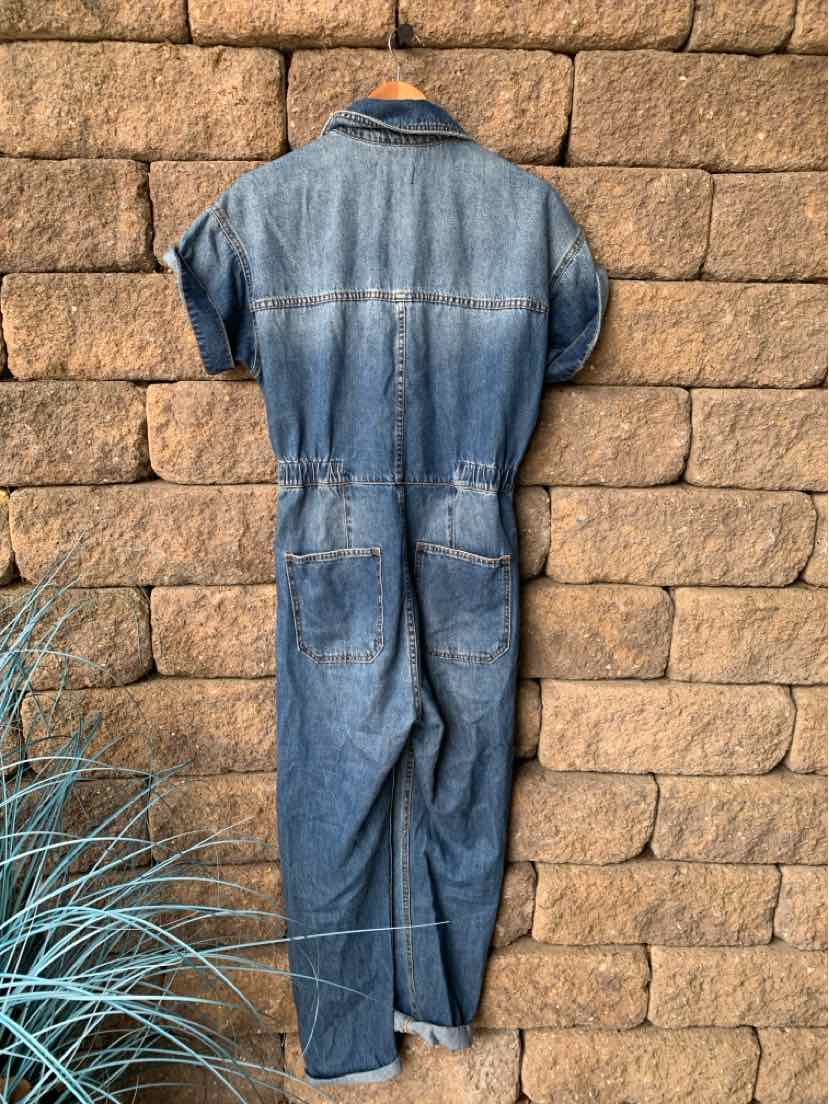 Blue denim short-sleeve jumpsuit with collar and back seam details hanging on a hook.