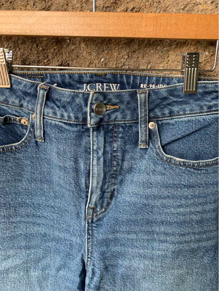 Blue high-waisted denim jeans with front button and zipper closure on wooden hanger.