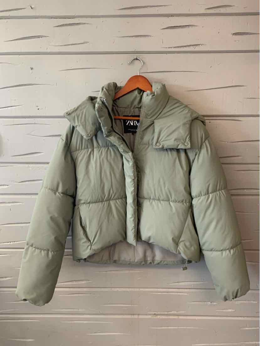 Light sage green quilted puffer jacket with a high collar, front zipper, and oversized flap pockets.