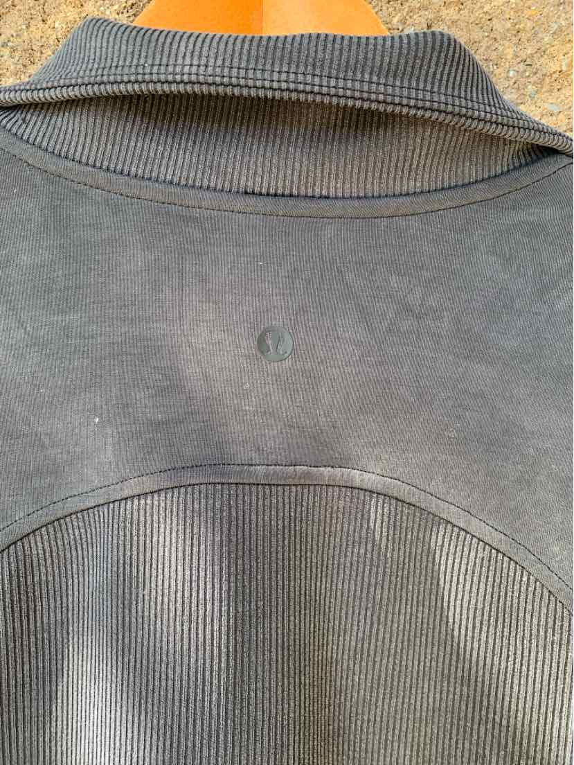 Dark gray ribbed fabric jacket back with smooth fabric upper panel and small reflective Lululemon logo centered below collar.