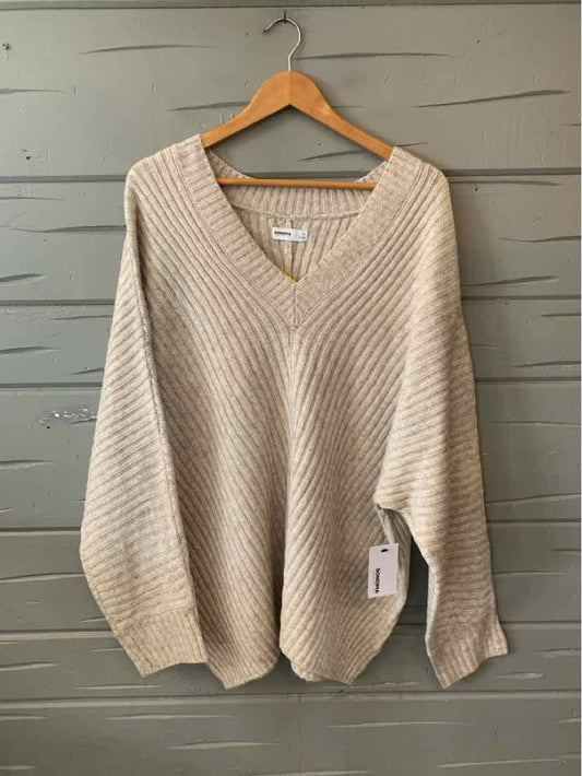 Tan oversized knit sweater with V-neck and long sleeves, size 1X, hanging on wooden hanger.