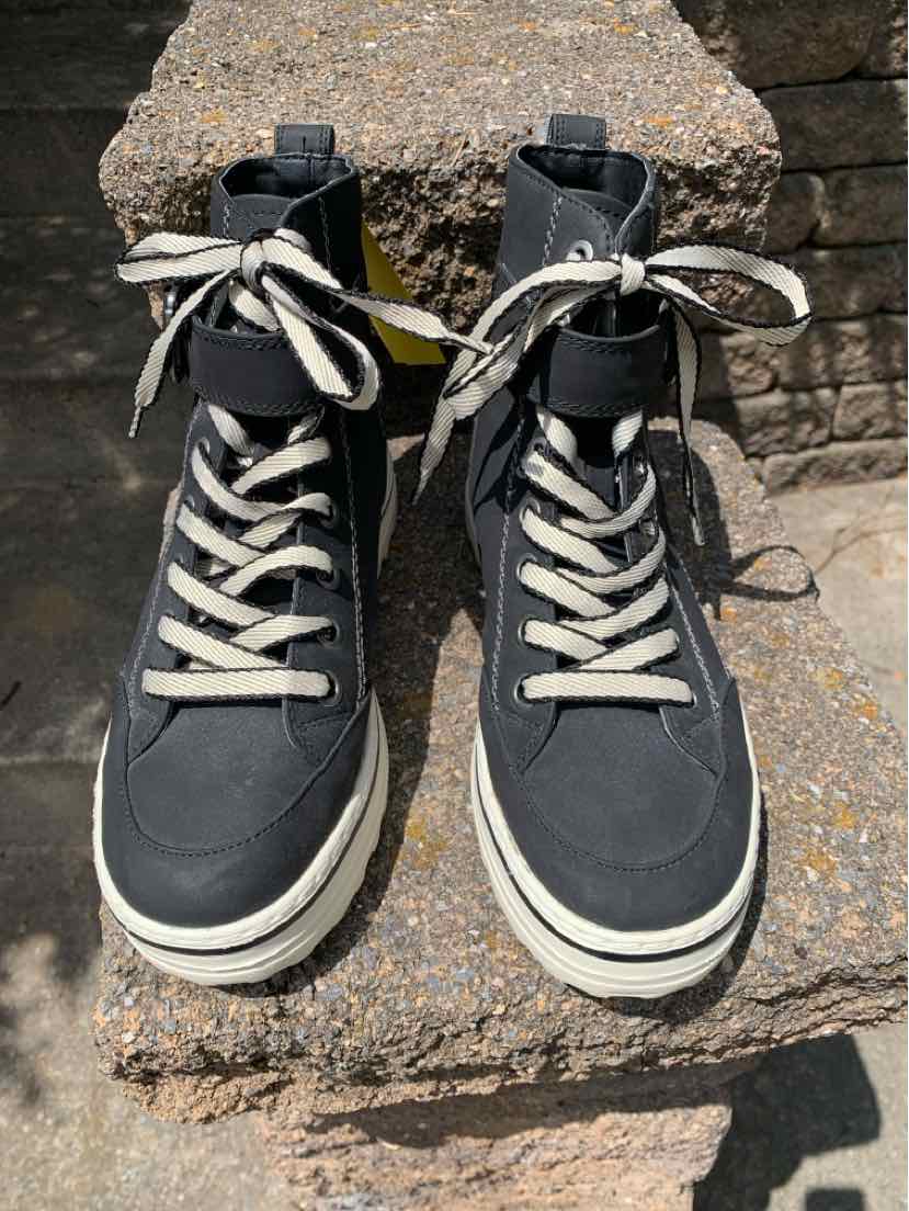 Black high-top sneakers with white laces and thick white soles on stone steps.