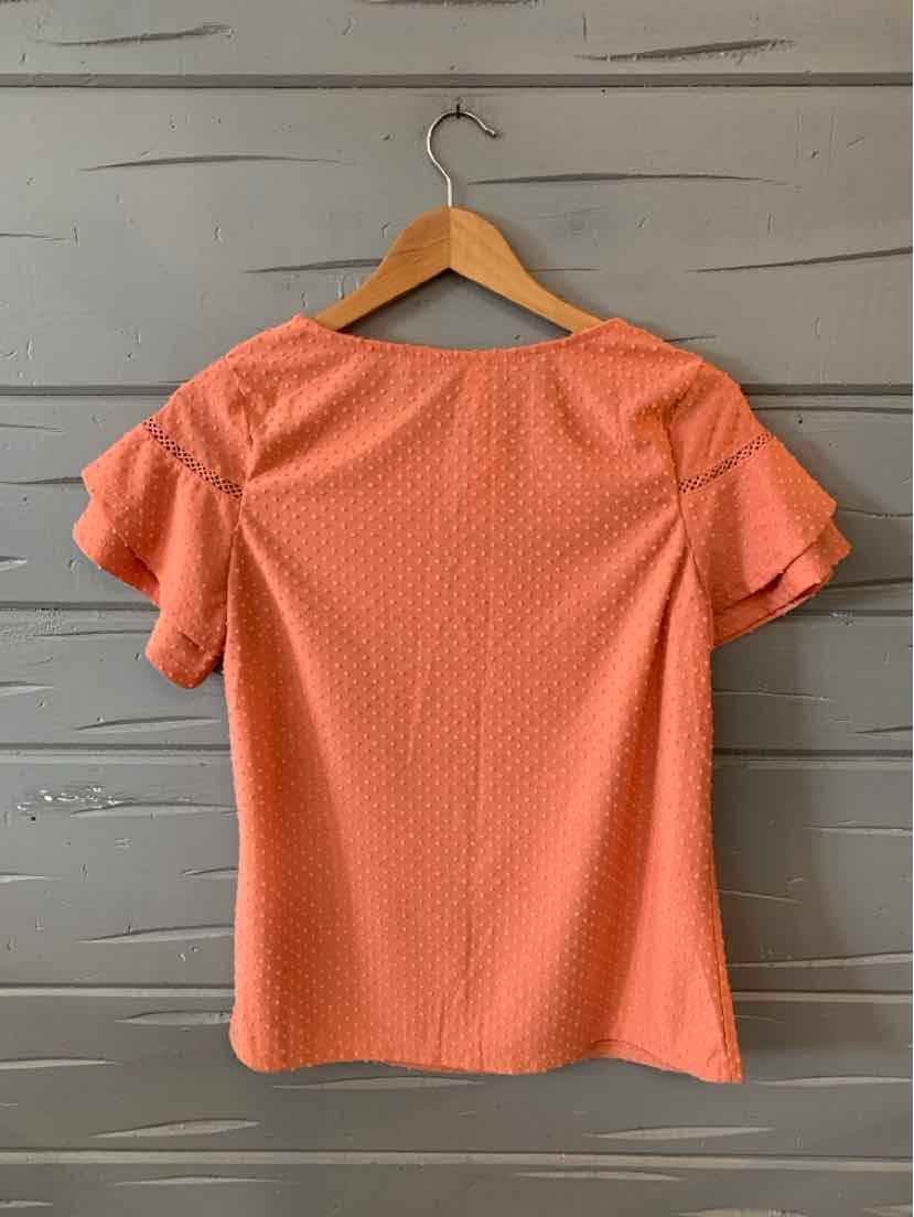 Coral orange short-sleeve blouse with textured polka dot pattern and ruffled sleeve edges on wooden hanger.
