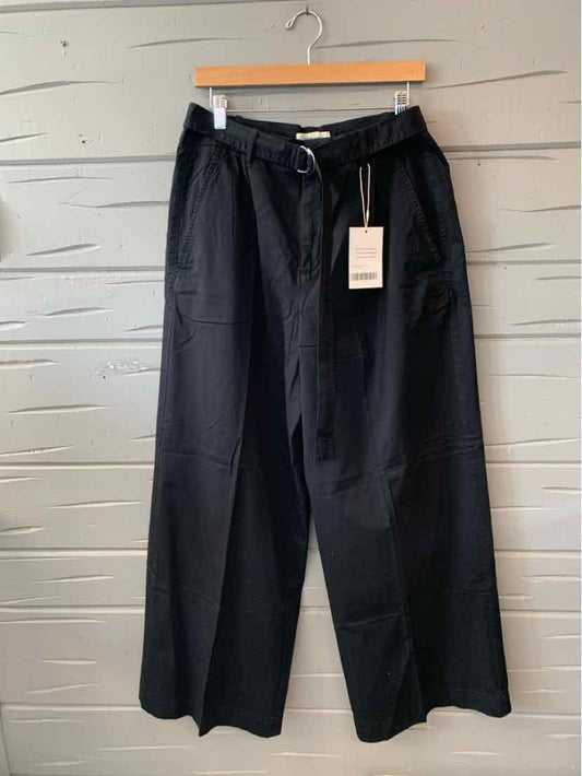 Black wide-leg pants with belt and front patch pockets hanging on wooden hanger.
