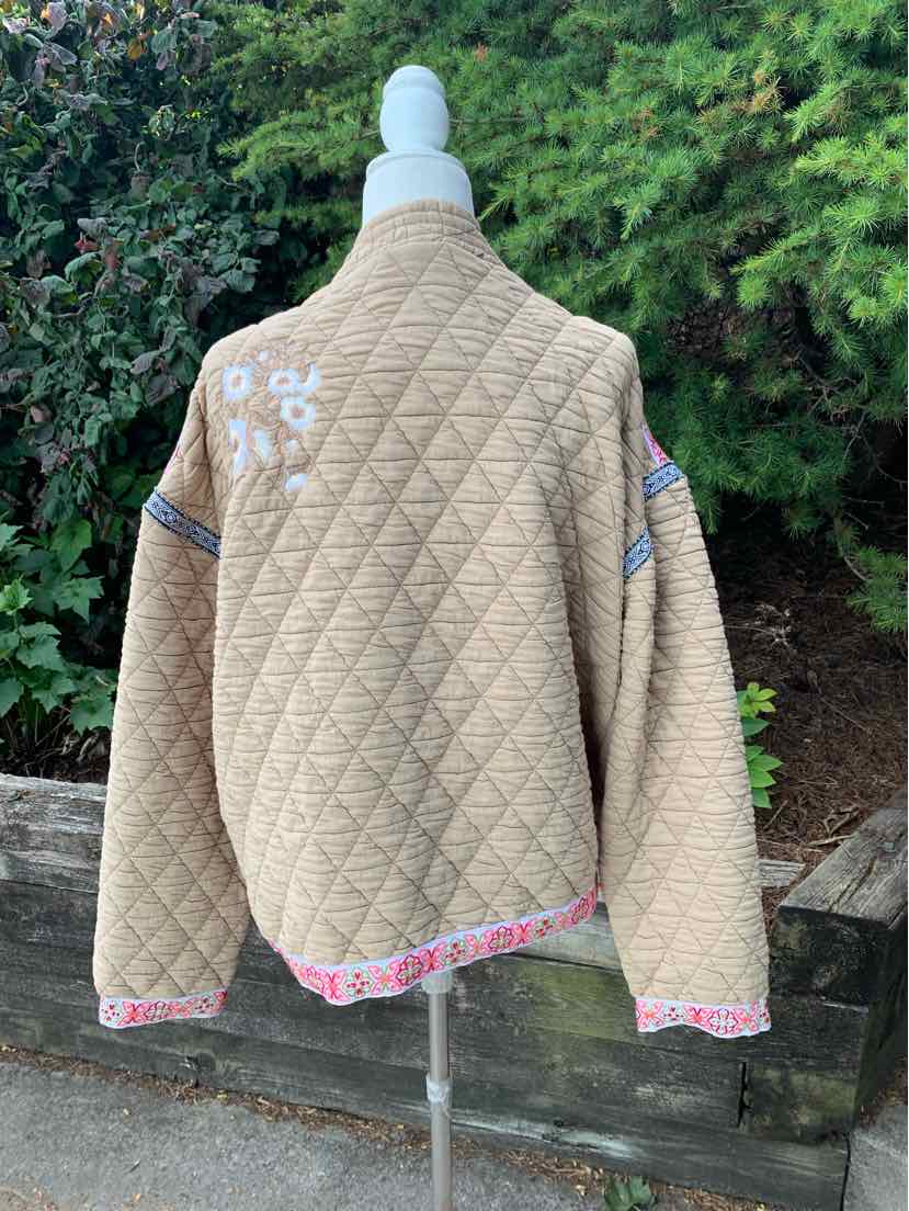 Tan quilted jacket with diamond stitching, floral embroidery on shoulder, and pink patterned trim.