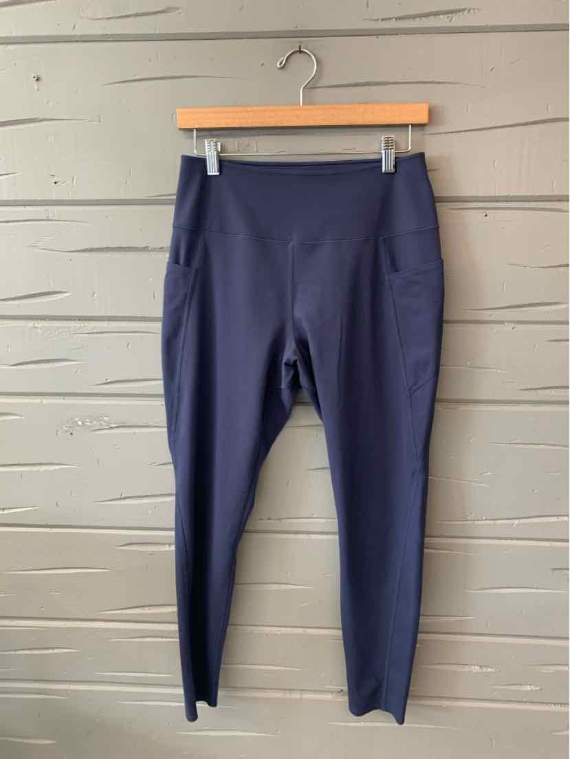 Navy blue high-waisted leggings with side pockets and slim ankle fit hanging on wooden hanger against gray wall.