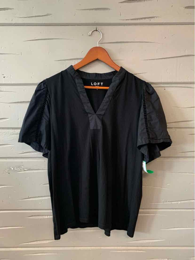 Black V-neck blouse with short puff sleeves on wooden hanger against light wood wall.