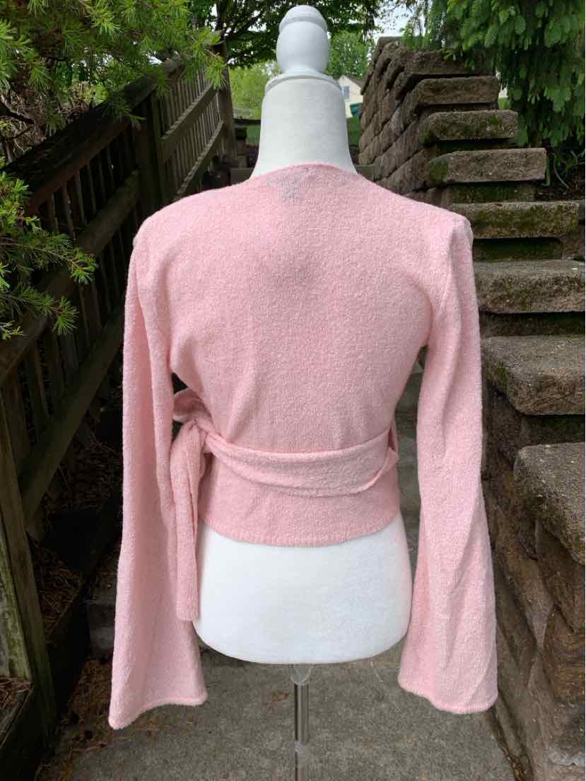 Light pink long-sleeve wrap top with soft fabric and fitted waist on white mannequin.