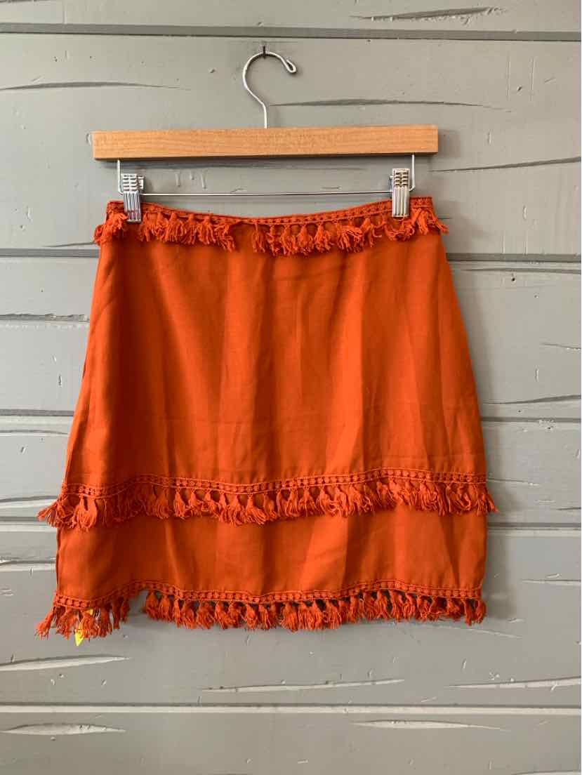 Rust-colored mini skirt with ruffled trim at waist, hem, and midsection, hanging on wooden hanger.