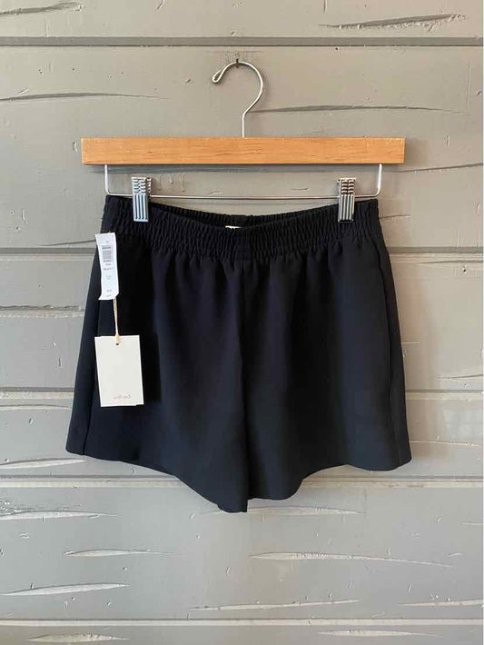 Black high-waist shorts with elastic waistband and side pockets, hanging on wooden hanger.