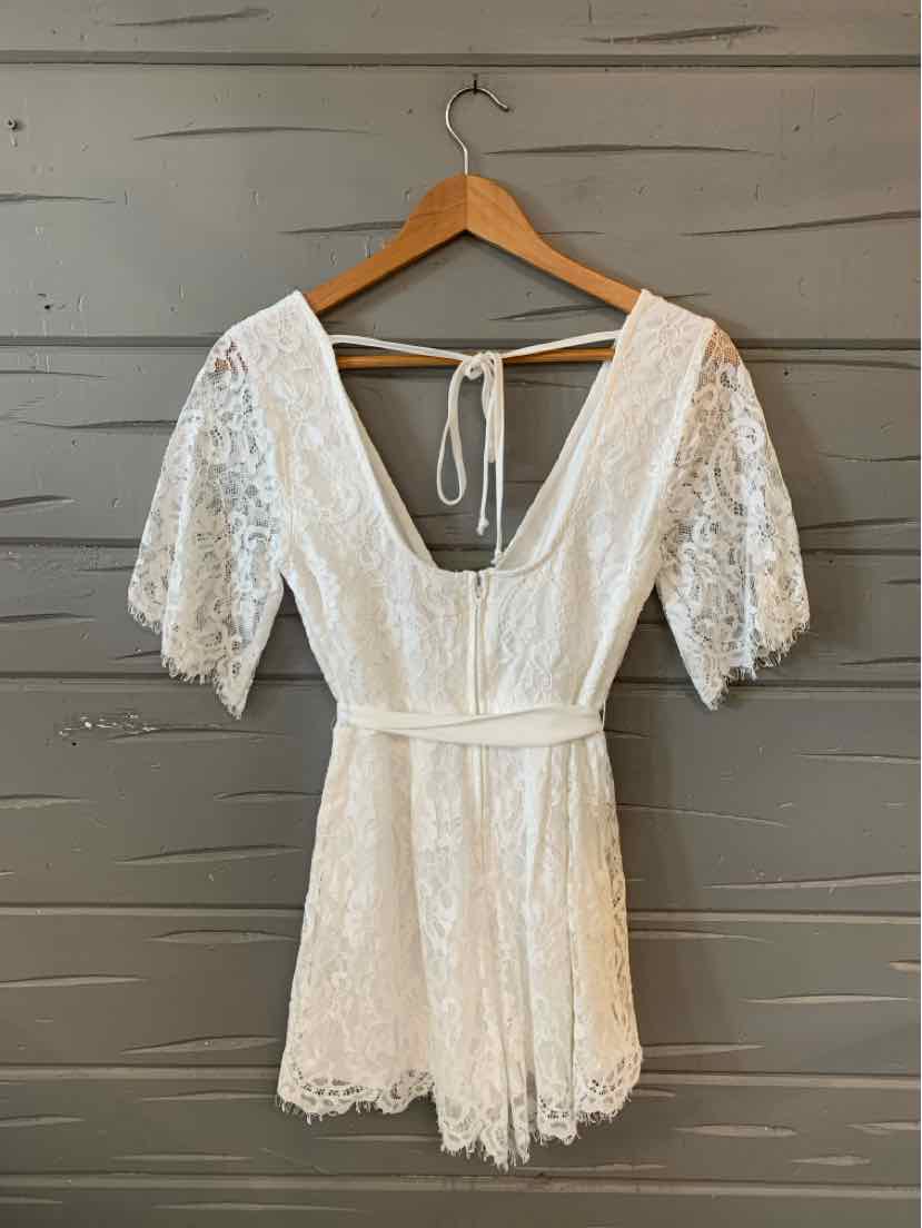 White lace romper with deep V-neck, tie-back, short puff sleeves, and scalloped hem.