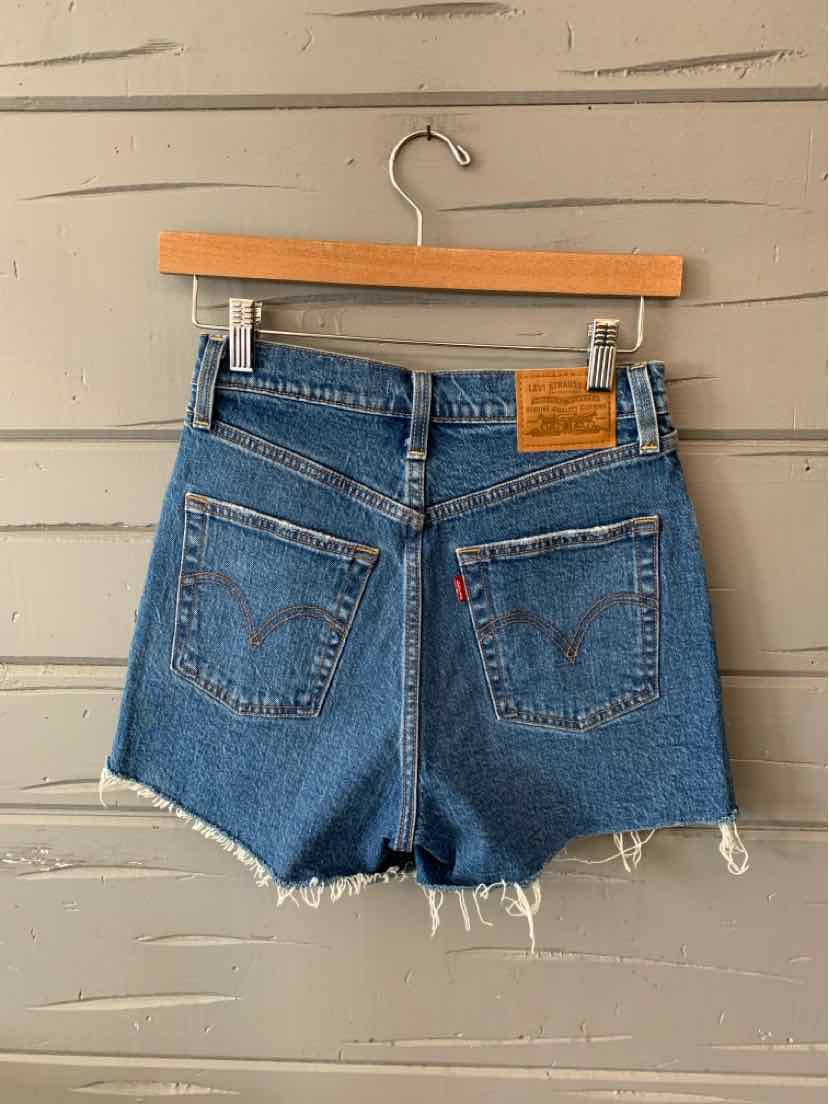 Blue denim Levi's shorts with frayed hems and back pockets, featuring a leather brand patch and red tag.
