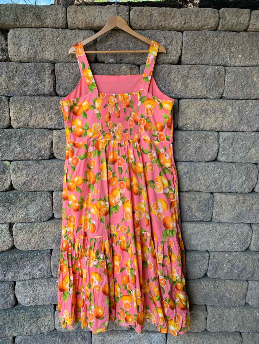Sleeveless midi dress with orange floral print and wide straps on coral background.