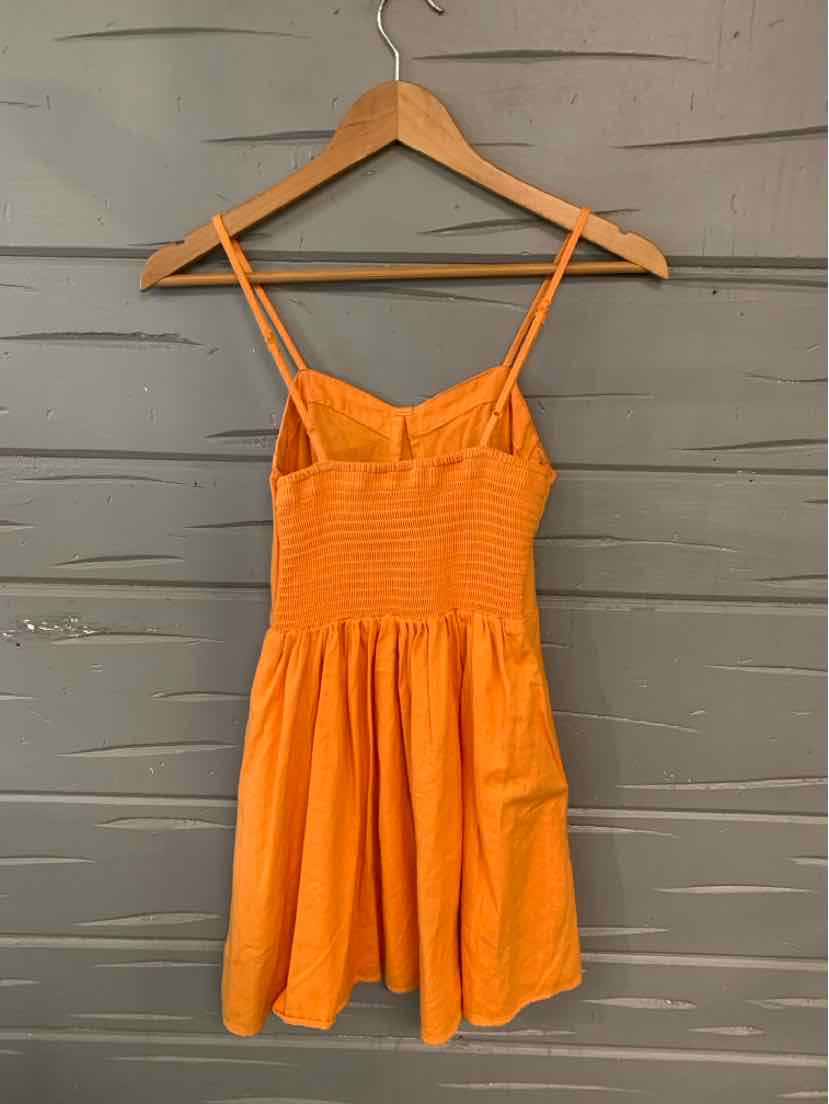 Orange sleeveless dress with smocked bodice and thin double straps on wooden hanger.