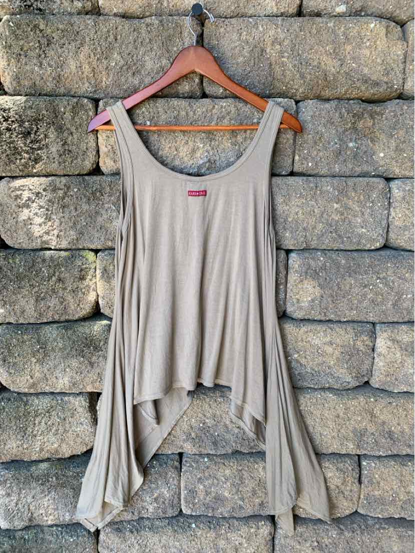 Light beige asymmetrical tank top with scoop neckline and flowy hem hanging on wooden hanger against stone wall.