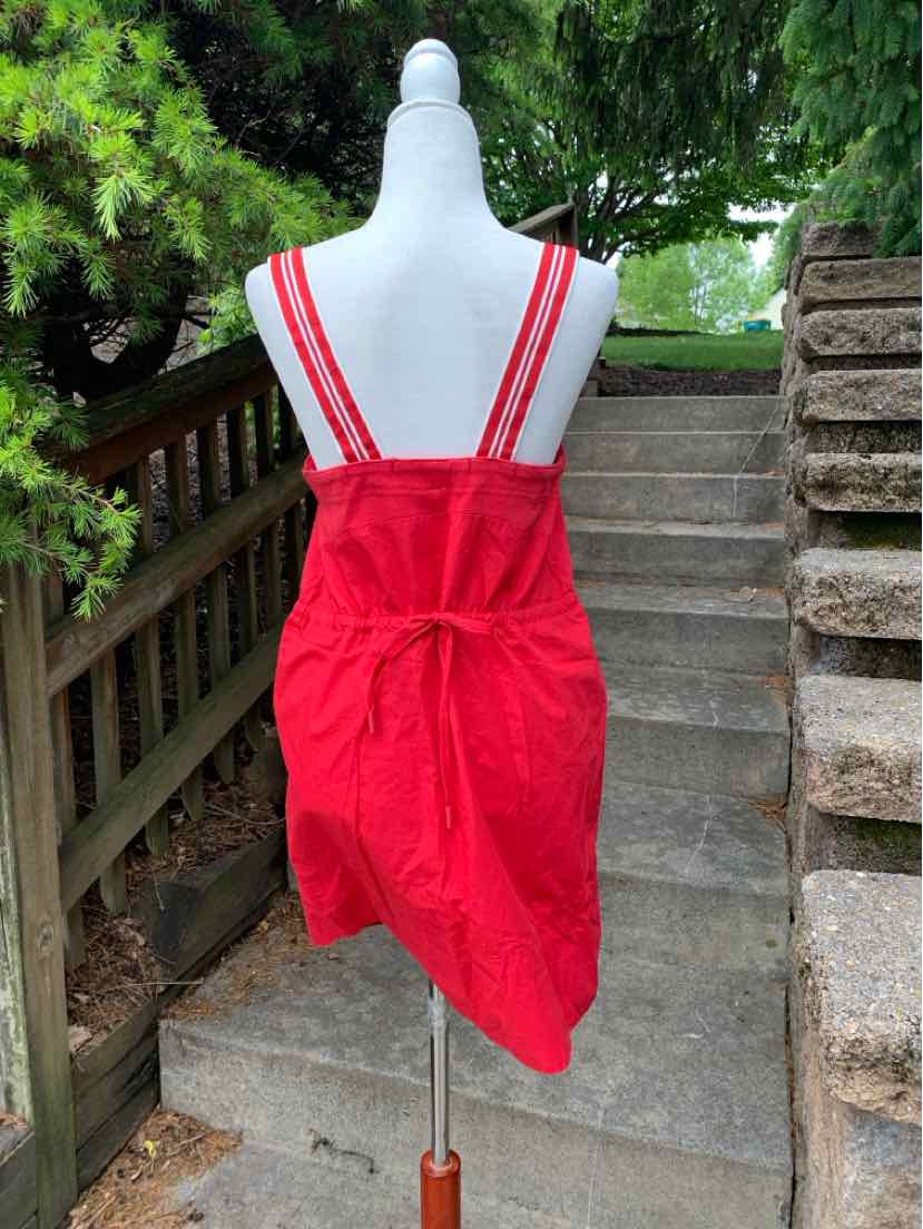 Red apron dress with adjustable shoulder straps and back tie detail on mannequin outdoors.