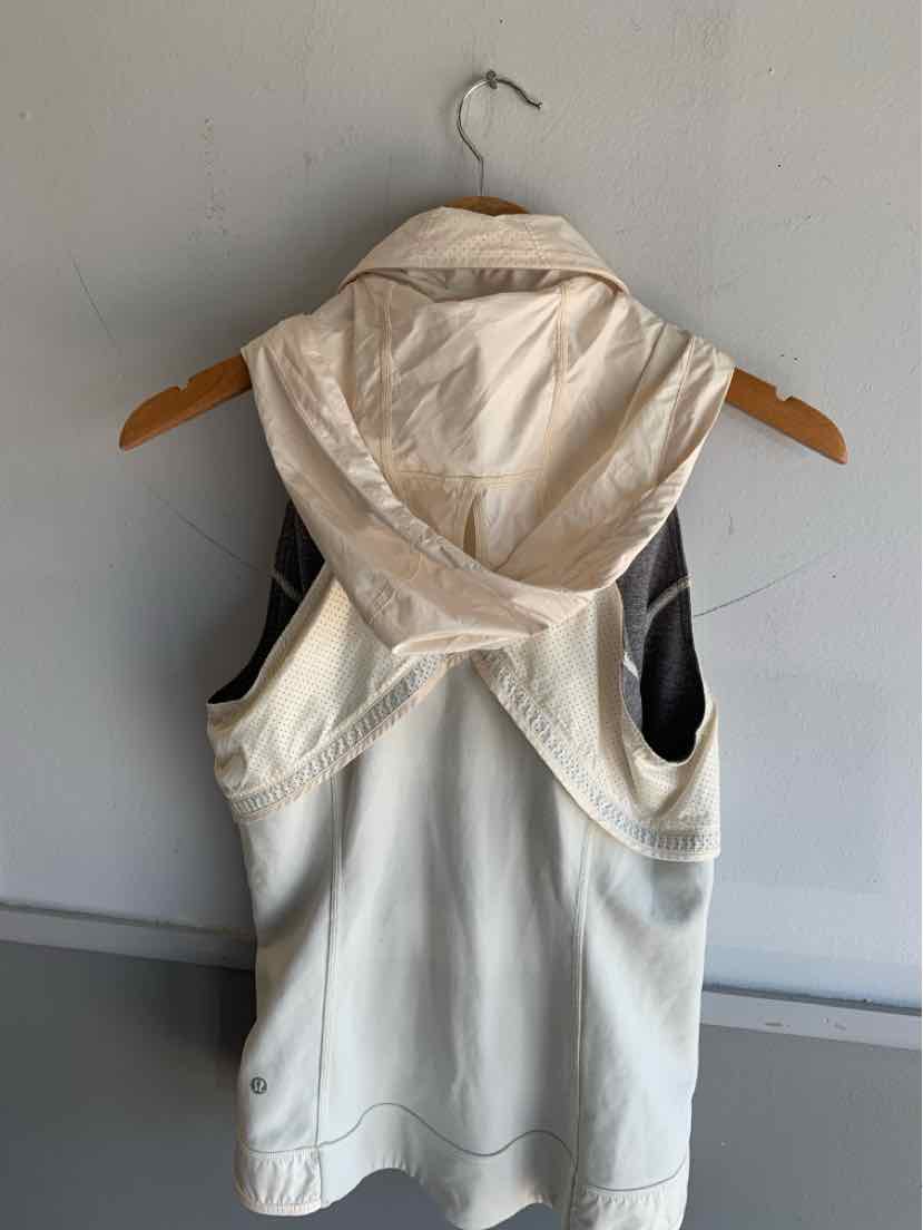 Light beige sleeveless hooded top with racerback design on wooden hanger against white wall.