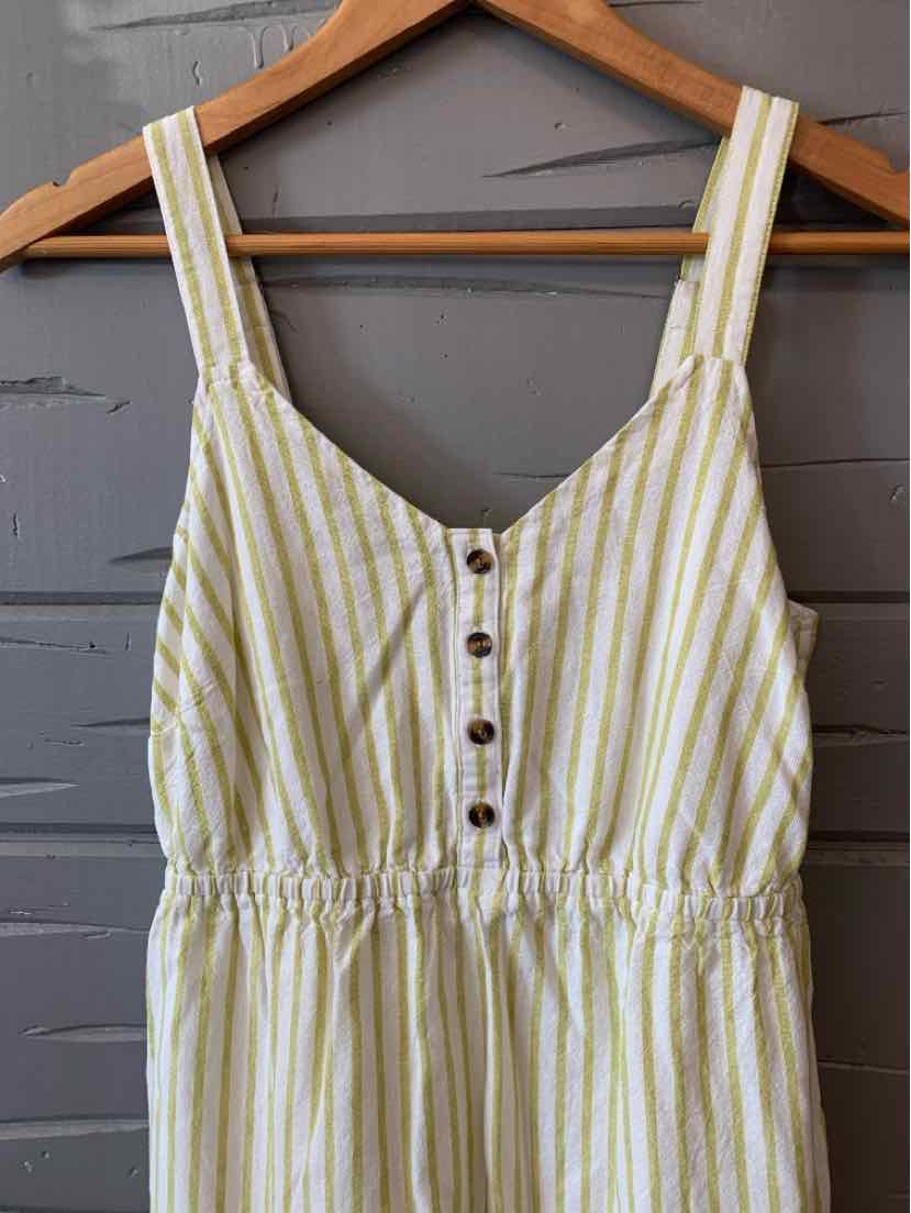 White dress with vertical green stripes, button front, elastic waist, and wide shoulder straps hanging on wooden hanger.