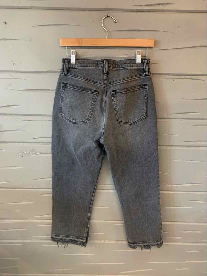 Black cropped jeans in size 6 with raw hem detailing and back pockets hanging on wooden hanger.