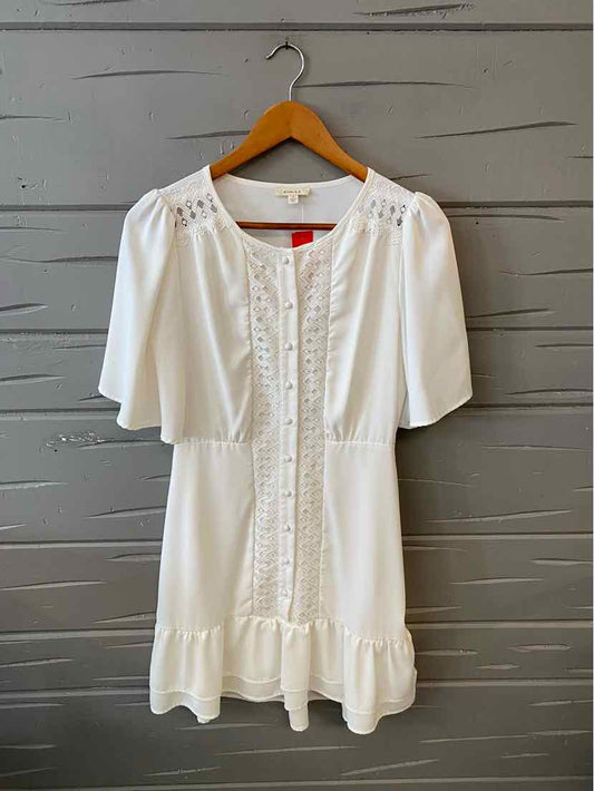 White short-sleeve dress with lace detailing down front and ruffled hem on wooden hanger.