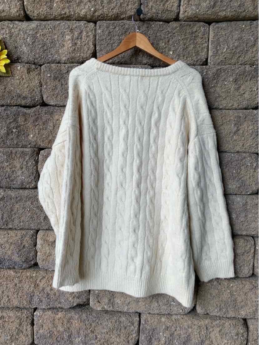 Cream white cable knit sweater with long sleeves and a crew neckline hanging on wooden hanger.