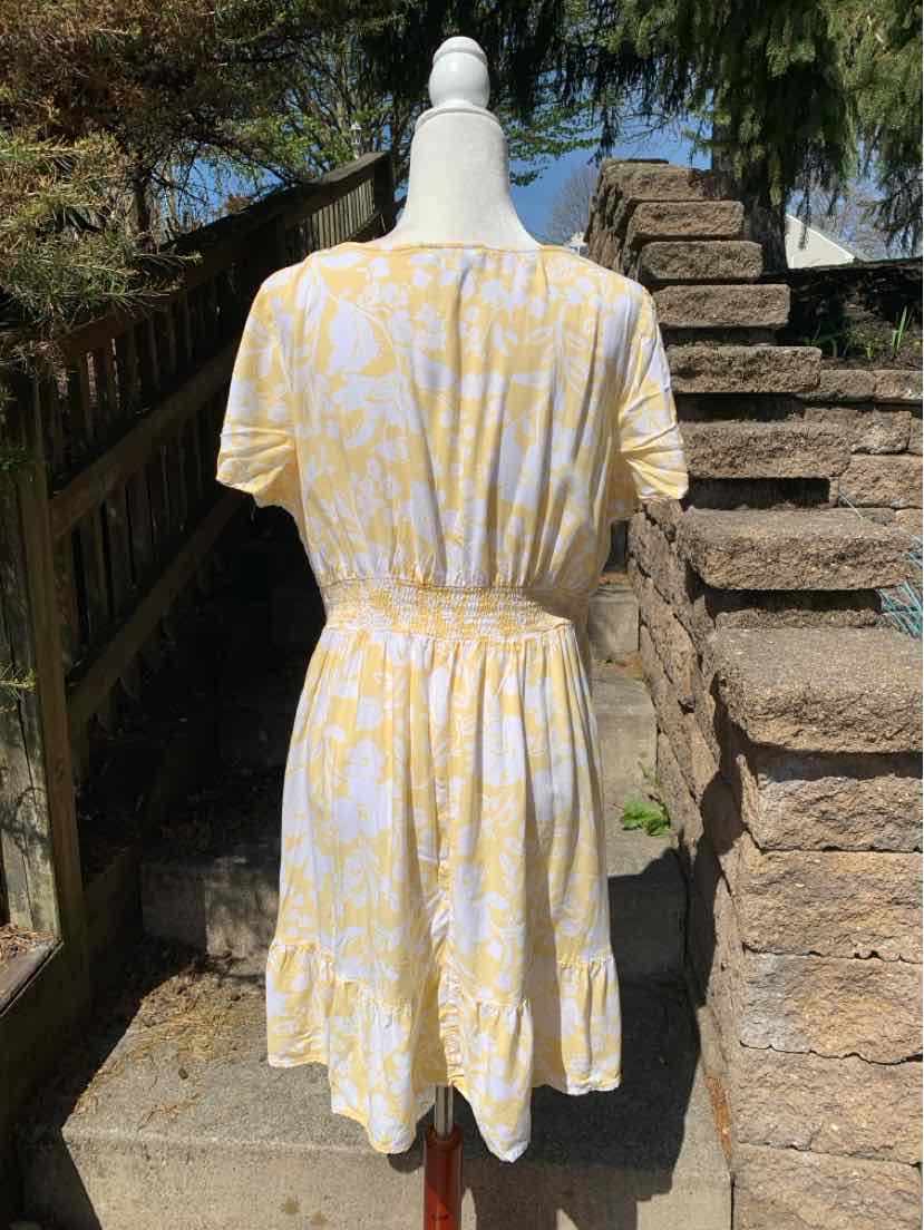 Yellow and white floral short-sleeve dress with elastic waist and knee-length hem shown from back.