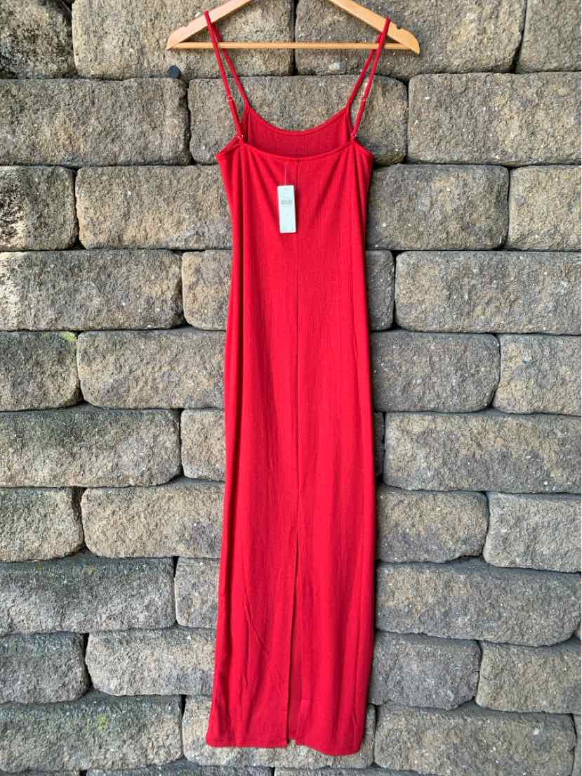 Red sleeveless midi dress with thin straps and fitted silhouette hanging on wooden hanger against stone wall.
