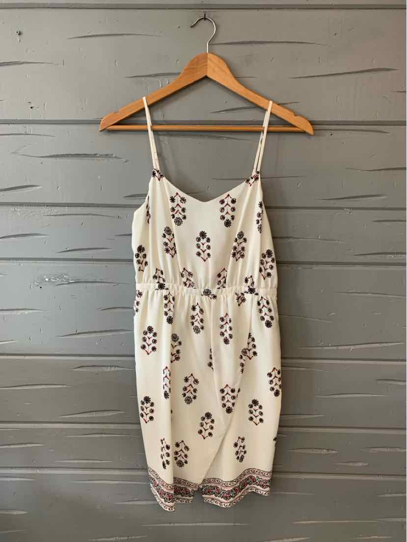 White sleeveless dress with thin straps, cinched waist, floral print, and patterned hem.