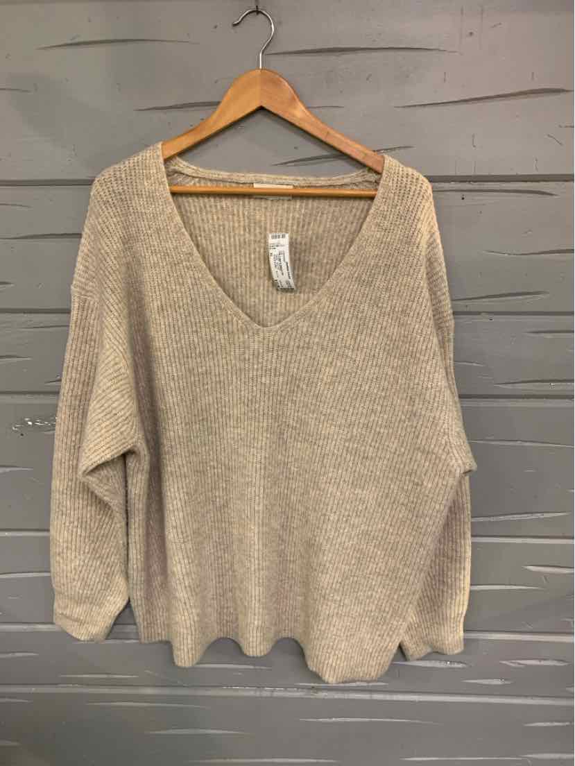 Tan oversized knit sweater with V-neck and long sleeves on wooden hanger.