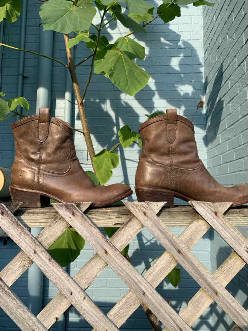 Pair of brown leather mid-calf boots with rounded toes and low stacked heels on wooden lattice fence.
