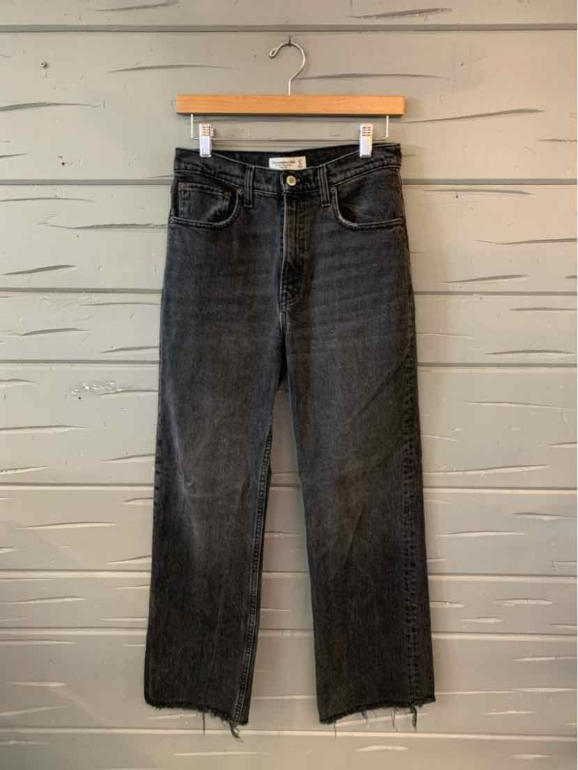 Black high-waisted denim jeans with a straight leg and raw hem detailing on a wooden hanger.