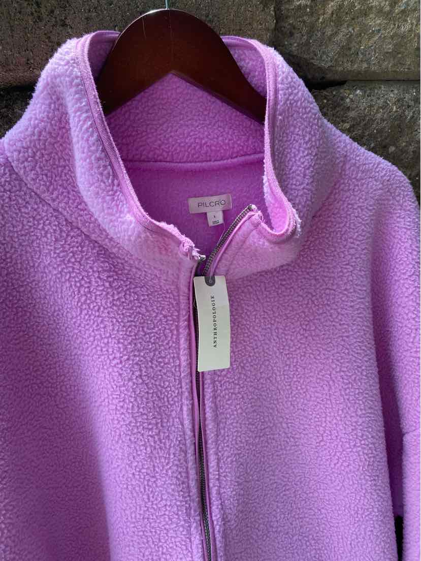 Lavender purple fleece zip-up jacket with collar, hanging on wooden hanger against stone background.