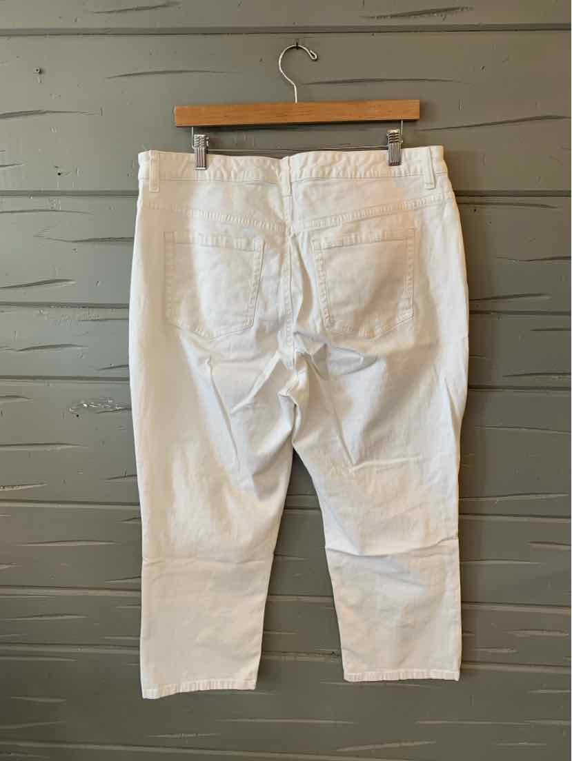 White high-waisted cropped pants with back pockets hanging on wooden hanger against gray wooden wall.