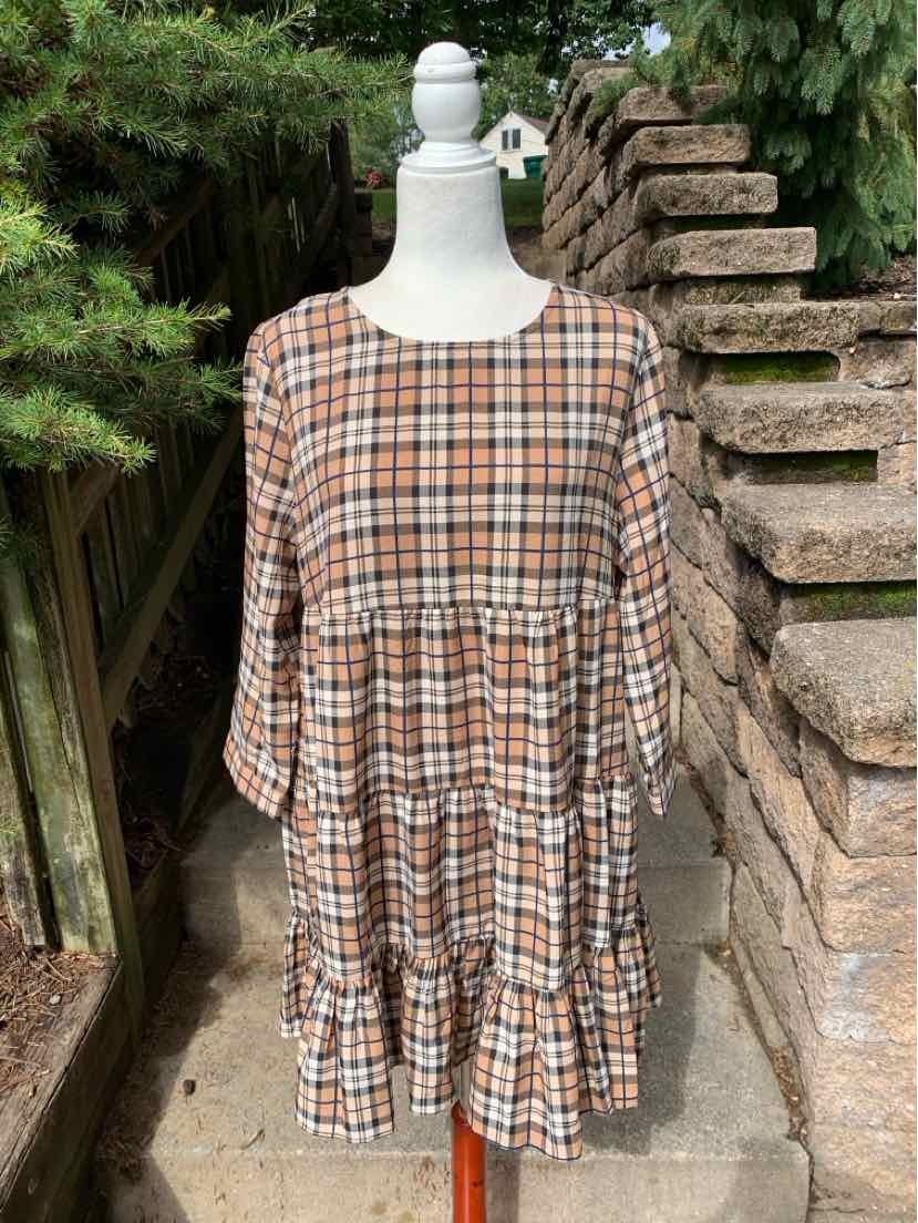 Brown and beige plaid long-sleeve dress with a round neckline and tiered skirt on a mannequin outdoors.
