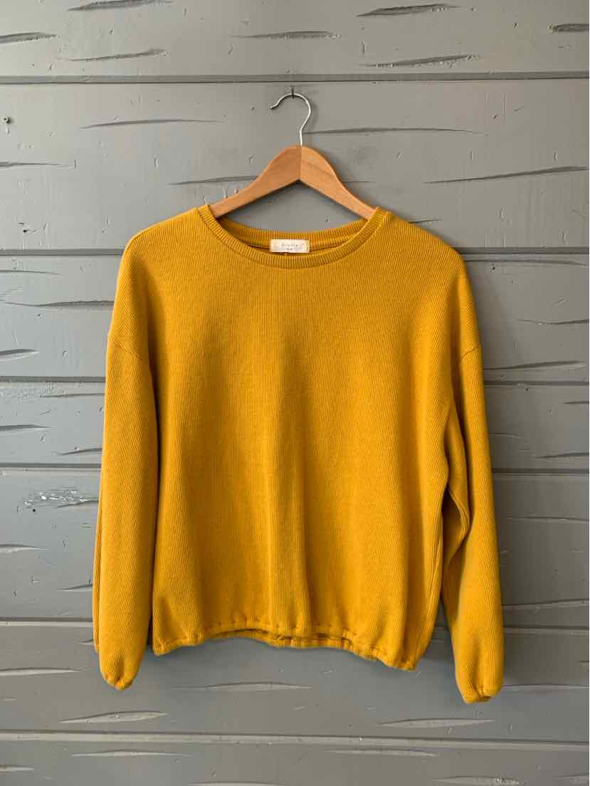 Mustard yellow crew neck sweater with long sleeves and relaxed fit hanging on wooden hanger.