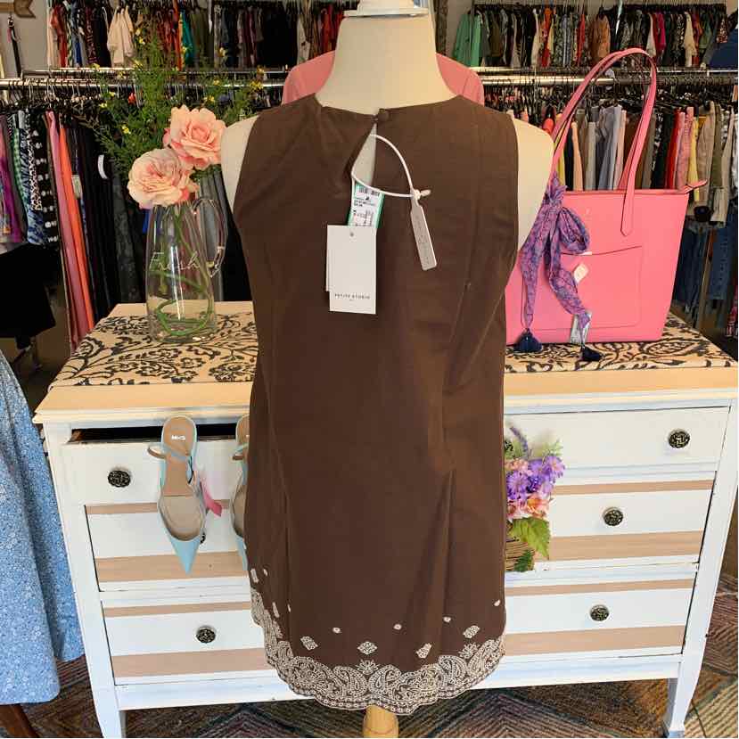 Brown sleeveless dress with white embroidered floral hem on mannequin.
