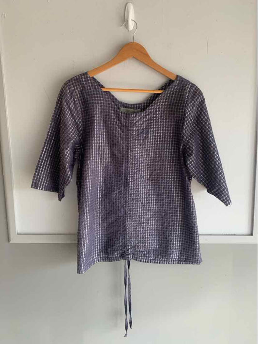Blue gingham check blouse with three-quarter sleeves and drawstring hem on wooden hanger.