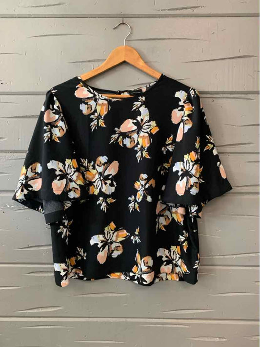 Black blouse with white and orange floral print and short sleeves hanging on wooden hanger.