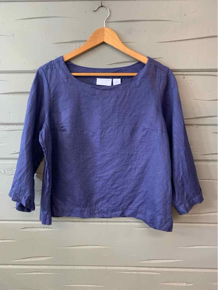 Blue linen long-sleeve top with scoop neck and relaxed fit hanging on wooden hanger.