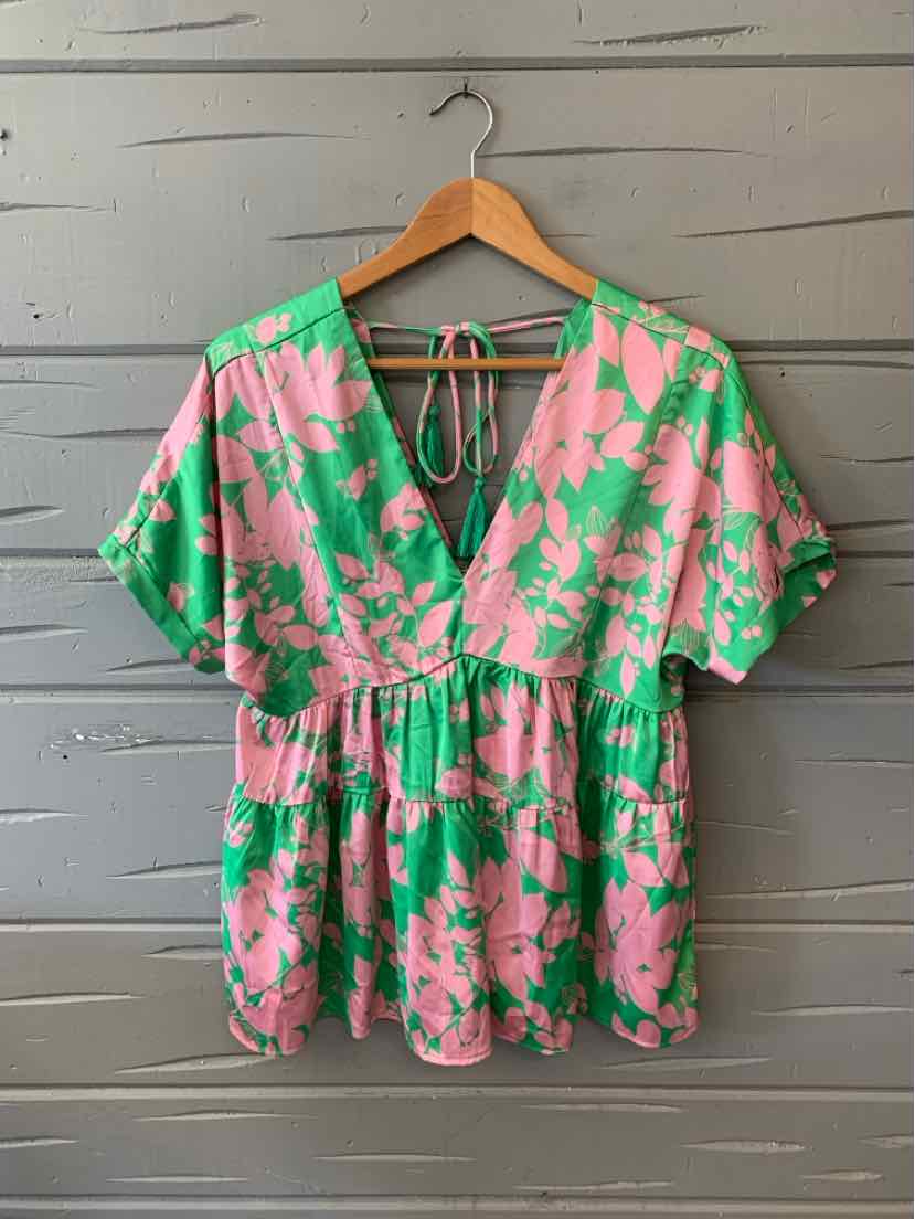 Pink and green floral short-sleeve blouse with deep V-neck and gathered waist on wooden hanger.