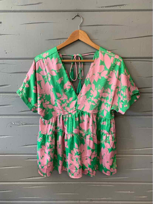 Pink and green floral short-sleeve blouse with deep V-neck and gathered waist on wooden hanger.