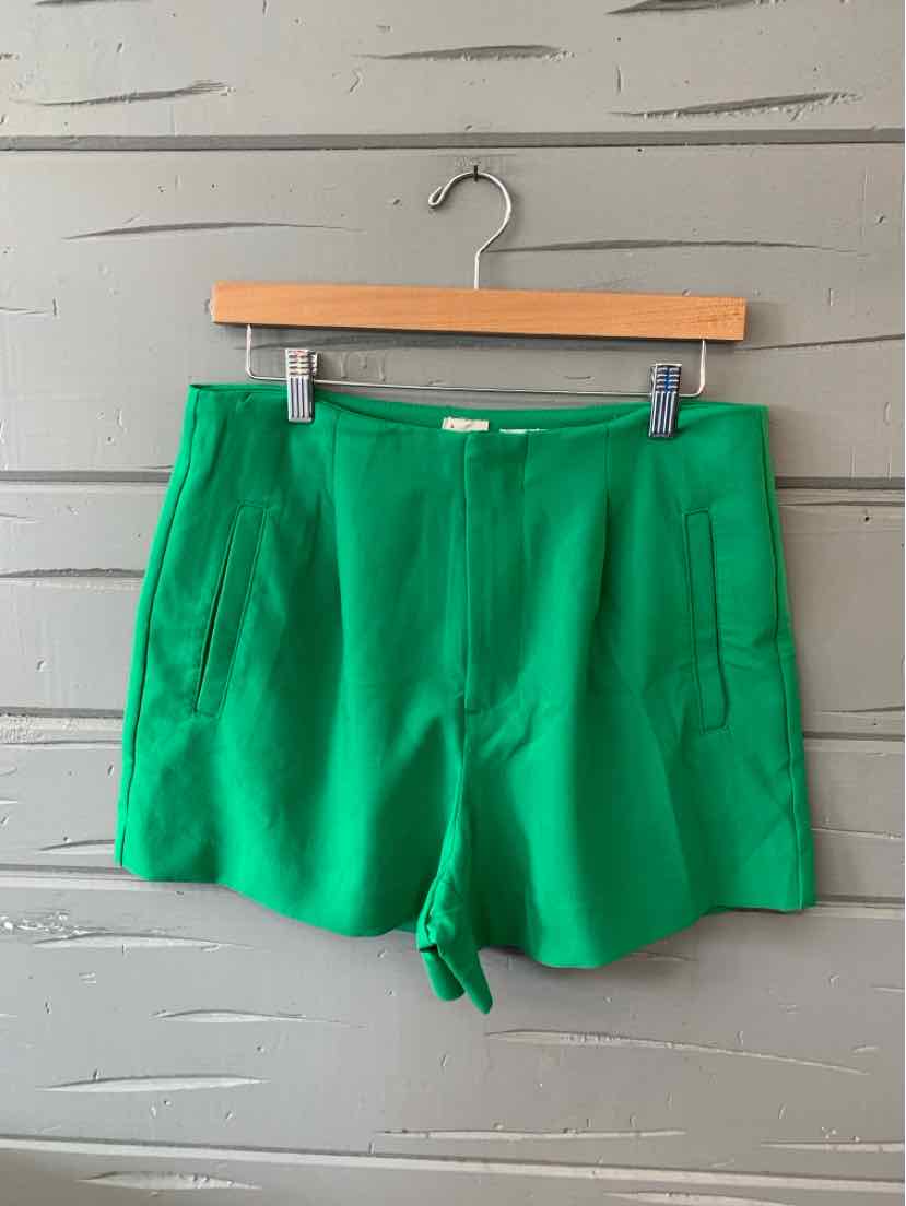 Bright green high-waist shorts with front patch pockets and a clean waistband hanging on wooden hanger.