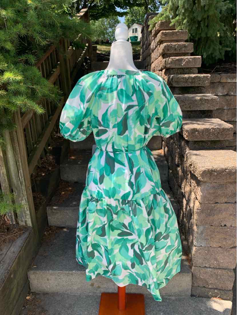 Green and white leaf print dress with puff sleeves and tiered skirt on a mannequin outdoors.