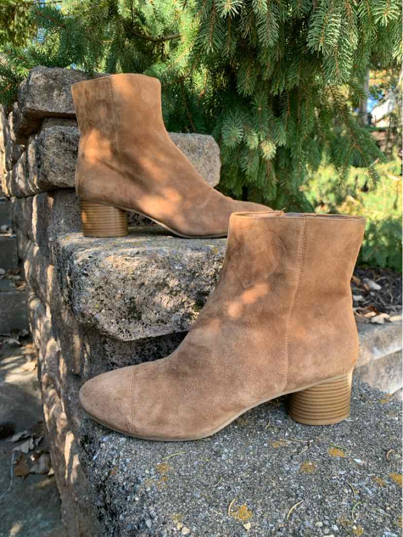Pair of tan suede ankle boots with rounded toes, side zippers, and stacked block heels on stone steps.
